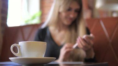 Kupa, arka planda bir akıllı telefon kullanan bir kadın odaklanmak bulanık.