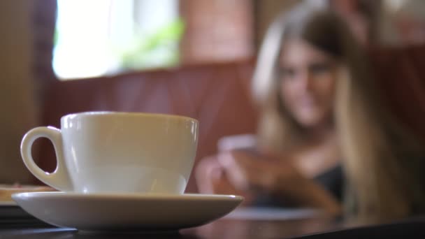 Сдвиг фокус с чашки белого кофе на молодую женщину с телефоном . — стоковое видео