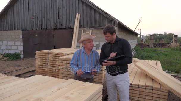Alter und junger Geschäftsmann, schaut auf ein Tablet, handelt über den Kauf von Holzbrettern — Stockvideo