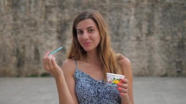 Sevimli genç kadın sokakta Kupası dondurma gelen bir kaşıkla yemek