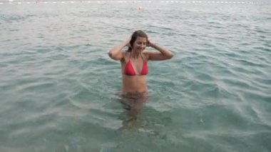 Genç kadın deniz, düzeltmeleri ve sıkar saç, kameraya bakarak dışarı gidiyor