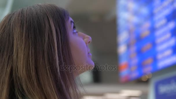 Unga kvinnan ser på informationstavlan avgångar på flygplatsen. — Stockvideo