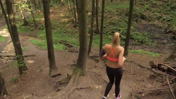 Сильная молодая женщина бежит по лесной тропе и спускается с холма — стоковое видео