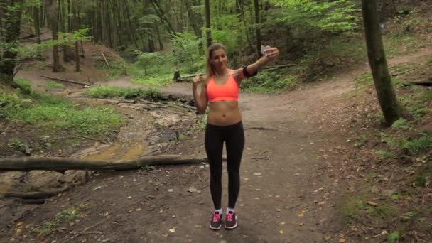 Atlética mujer en correr ropa hace un selfie de sí mismo en un bosque camino — Vídeos de Stock