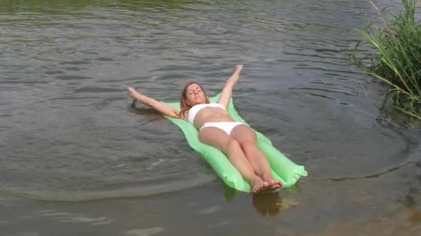 Jeune femme bronzée dans un bikini blanc flottant dans la rivière sur le matelas . — Video