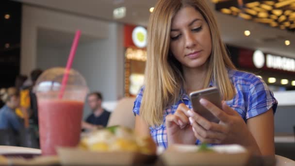 在蓝色格仔恤衫年轻可爱的女人坐在咖啡厅使用智能手机 — 图库视频影像