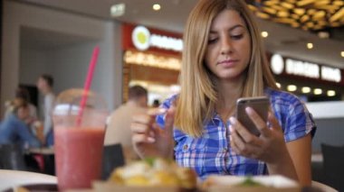 Genç kadın içecekler suyundan tüp bir Smartphone kullanarak Cafe güzel