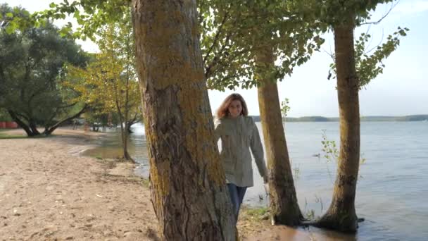 Mujer coqueta mira desde detrás de un árbol y sonríe jugando a esconderse y buscar — Vídeos de Stock