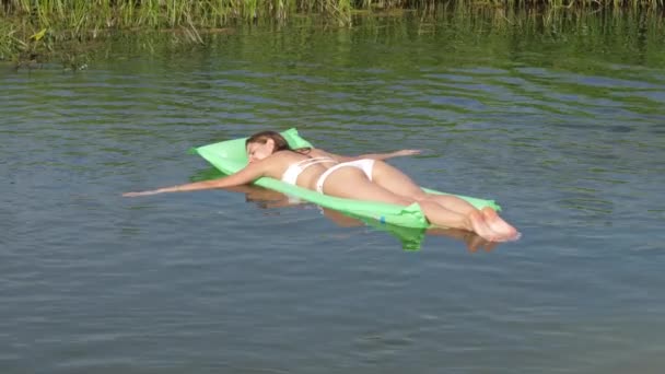 Die schöne, braun gebrannte Frau im weißen Bikini schwimmt auf der Matratze im Fluss. 4k — Stockvideo