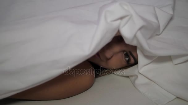 Cute Woman Looks Out From Under The Covers Smiling Winking Eye Shows Language — Stock Video