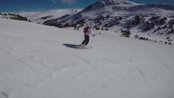 Una mujer esquiando en una pista de esquí, el sol y las montañas nevadas . — Vídeos de Stock