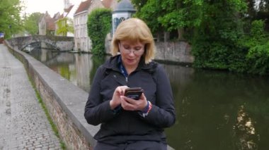 Bir kadın tarafından nehir kanalı oturur ve telefon mesaj çevirir.