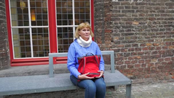 坐在长凳上的女人有一个红色的袋子有一个红色的窗口, 看到的景点. — 图库视频影像