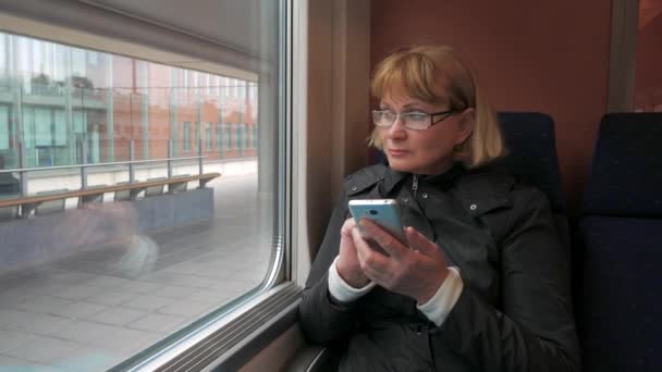 Donna in occhiali seduta sul treno e quadranti con le dita al telefono . — Video Stock