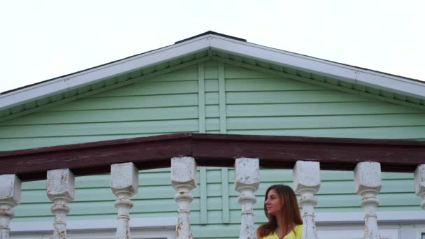 Красива жінка в жовтій сукні йде на балкон і тримає перила . — стокове відео