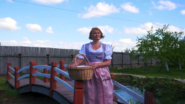 A woman in a national costume is standing by a beautiful bridge across a pond. — Stock Video