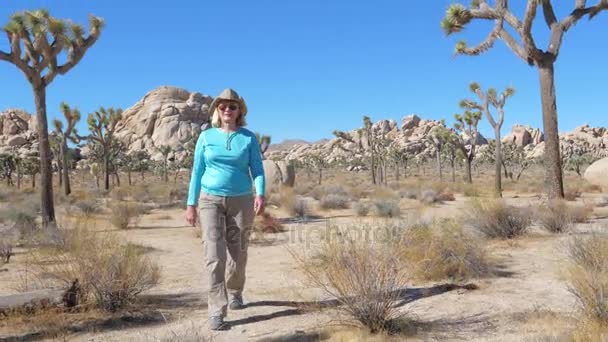 Donna col cappello da cowboy cammina nel bel mezzo del deserto del Mojave, agitando la mano — Video Stock