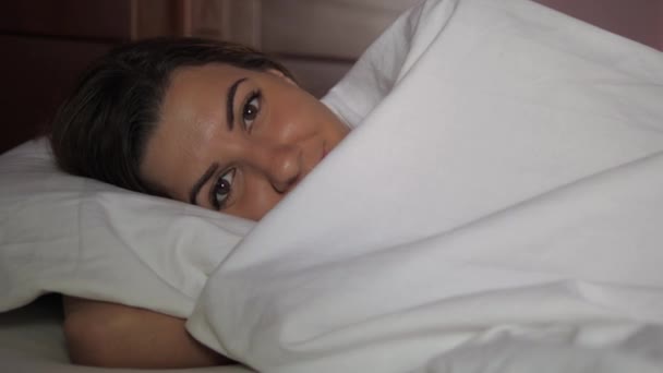 Εύθυμος μελαχρινή νεαρή γυναίκα ξαπλωμένη στο κρεβάτι, διασκέδαση, καλύπτει τα μάτια και το χαμόγελο — Αρχείο Βίντεο
