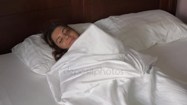 Брюнетка жінка лежить в ліжку під обкладинки, pulls ковдра має веселощі посміхаючись — стокове відео