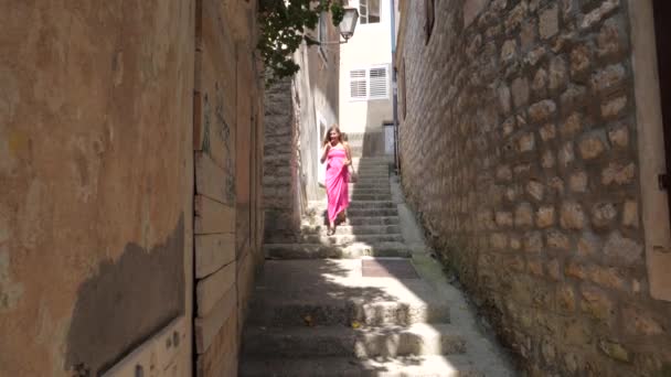 Femme dans une robe rose descend les escaliers de la rue étroite vieille pierre — Video