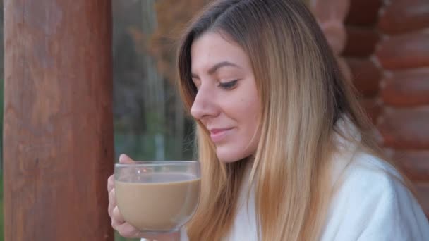 Primer plano de la mujer en el albornoz bebiendo café caliente en el porche de una casa de madera — Vídeos de Stock