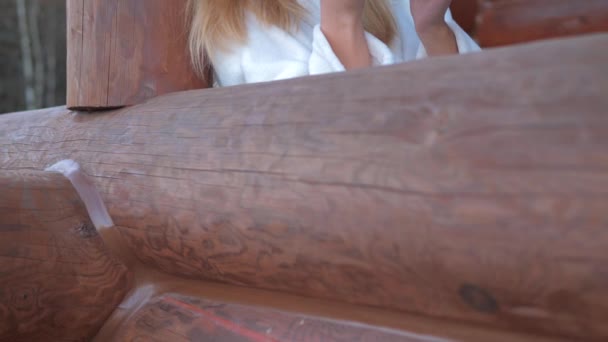 Крупним планом жінка в халаті п'є гарячу каву на веранді дерев'яного будинку — стокове відео