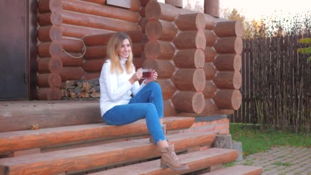 Giovane donna seduta sui gradini del portico della casa di legno e bere tè — Video Stock