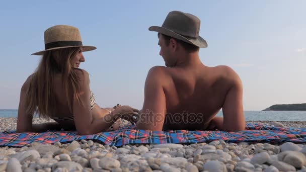 Feliz jovem casal tomando banho de sol na praia, deitado de costas e beijos — Vídeo de Stock
