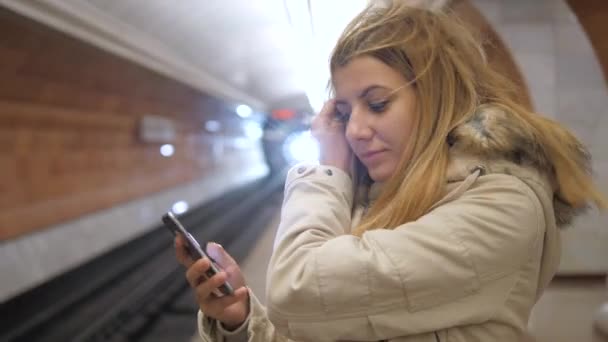 Attraktiv kvinna stående i metro och med smartphone, väntar på ett tåg. — Stockvideo