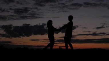 Romantik Çift, günbatımında elele etrafında döne döne karanlık siluet