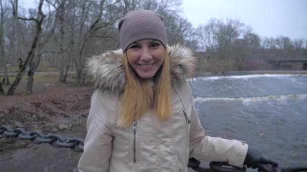 Femme en vêtements chauds souriant debout sur le pont suspendu sur la rivière — Video