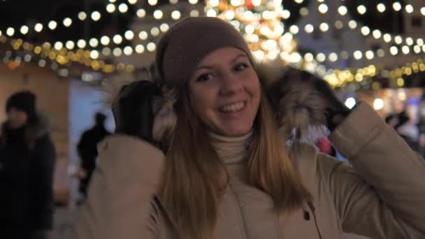 Mulher de Vestuário Quente Sorrindo, em pé no Mercado de Natal com Iluminações — Vídeo de Stock