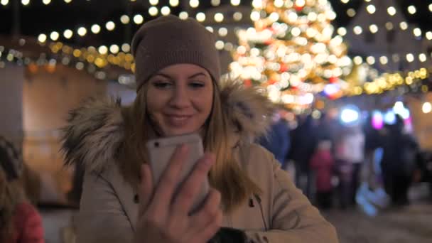 Selfie joven mujer sonriente, de pie en el mercado de Navidad con iluminaciones — Vídeos de Stock