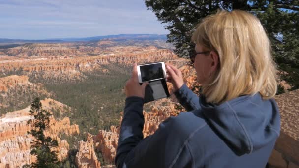 Kvinna turist står på utsiktsplatsen i Bryce Canyon och foton till Smartphone — Stockvideo