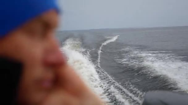 Primer plano borrosa cara hombre con brillante sombrero azul, barco flotante rápidamente en el mar — Vídeos de Stock