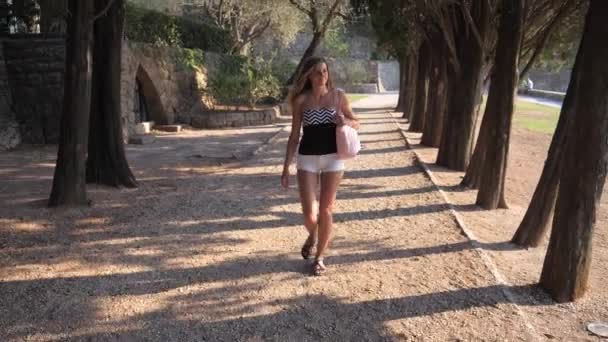 Movimiento joven atractiva mujer turista caminando a lo largo de callejón árboles en las sombras 4K — Vídeo de stock