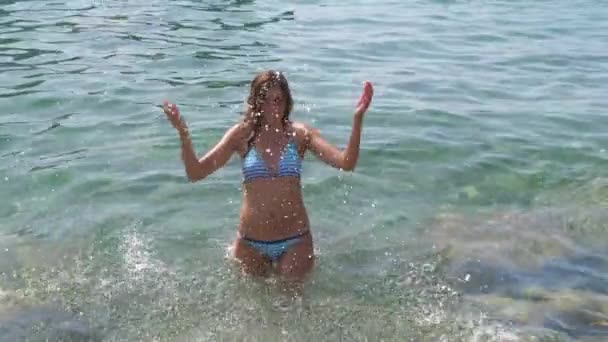 Mujer bronceada joven en bikini en cintura profunda en el mar azul salpica las manos de agua — Vídeo de stock