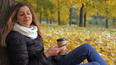 Sarı sonbahar yaprakları, ağacında arkası oturan kadın kullanır Smartphone
