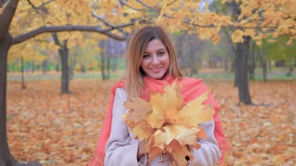 穿着米色外套和橙色围巾的女士捧着花束黄色的秋叶 — 图库视频影像