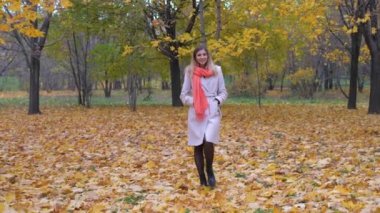 Bayan bir bej bir palto ve turuncu eşarp sonbahar halıda sarı yaprakları yürüyüş