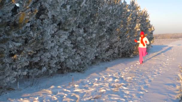 Mujer en invierno corriendo a la nieve al atardecer, sonriendo y agitando su mano — Vídeo de stock