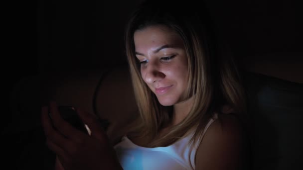 Mujer en la oscuridad usando Smartphone antes de acostarse, cara iluminada desde la pantalla — Vídeos de Stock