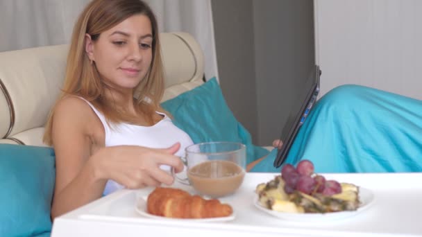 Femeie tânără cu laptop care mănâncă micul dejun în pat acasă și bea cafea . — Videoclip de stoc