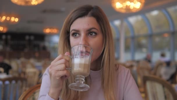 Mulher no café bebendo café de uma palha olha sonhadamente para fora da janela na rua — Vídeo de Stock