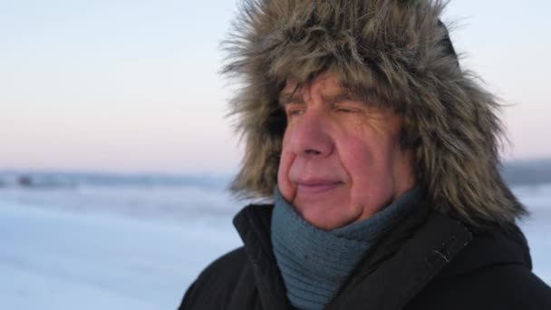 Портрет літнього чоловіка зі зморшками в куртці та капелюсі на відкритому повітрі взимку — стокове відео