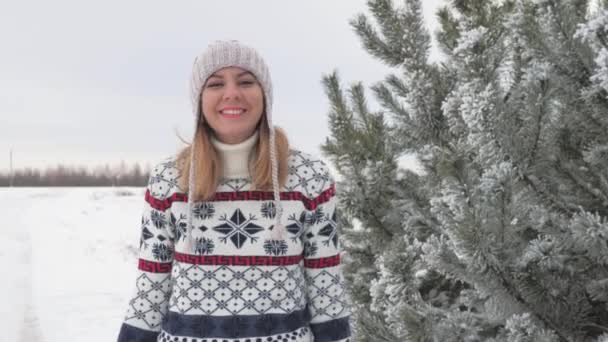 Bewegung einer lächelnden schönen Frau, die im Winter im Schnee entlang der Tanne spaziert — Stockvideo
