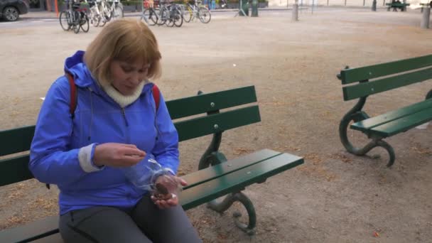 Женщина сидит на скамейке на улице и ест сладости из упаковки — стоковое видео