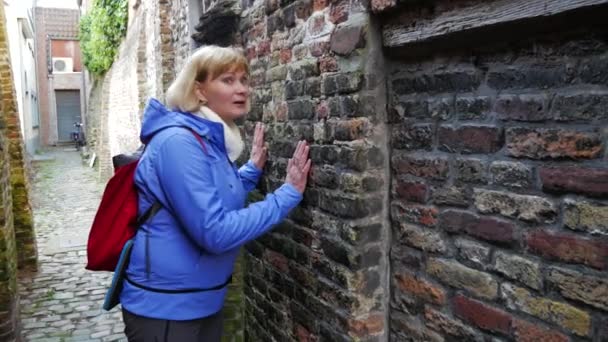 Туристка прикладывает ухо к каменной стене и слушает музыку — стоковое видео