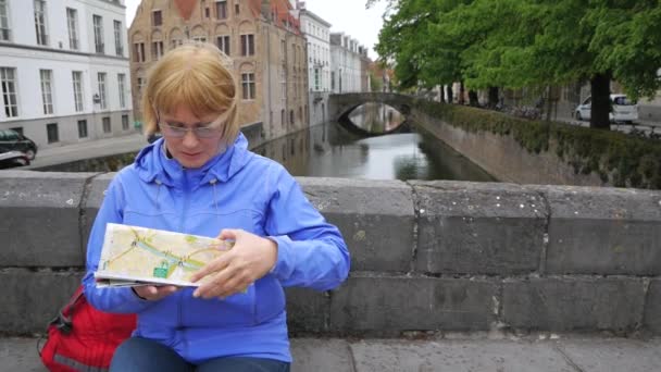 Touristin sitzt auf Brücke des malerischen Wasserkanals und studiert Stadtplan — Stockvideo