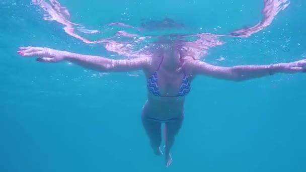Подводный вид молодой женщины в купальнике плавает в синем море — стоковое видео